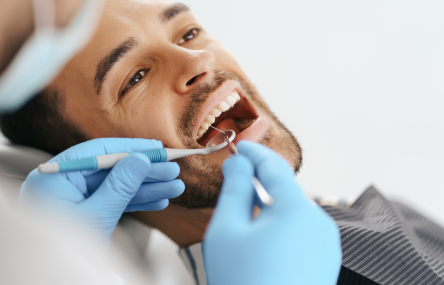 A man getting a dental check-up, with a dentist using dental tools inside his mouth.